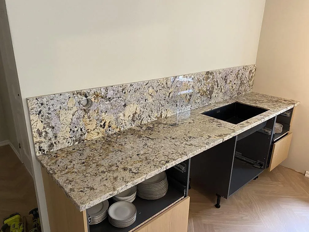 Väggbänk i polerad Alaskan white granit med svart diskho, stänkskydd och öppna köksstommar i Höllviken.