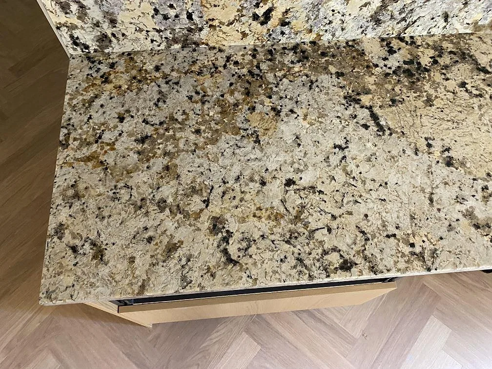 Ytnära bild av polerad Alaskan white granit på köksbänk med kraftig spräcklighet och varm grå teckning i Höllviken.
