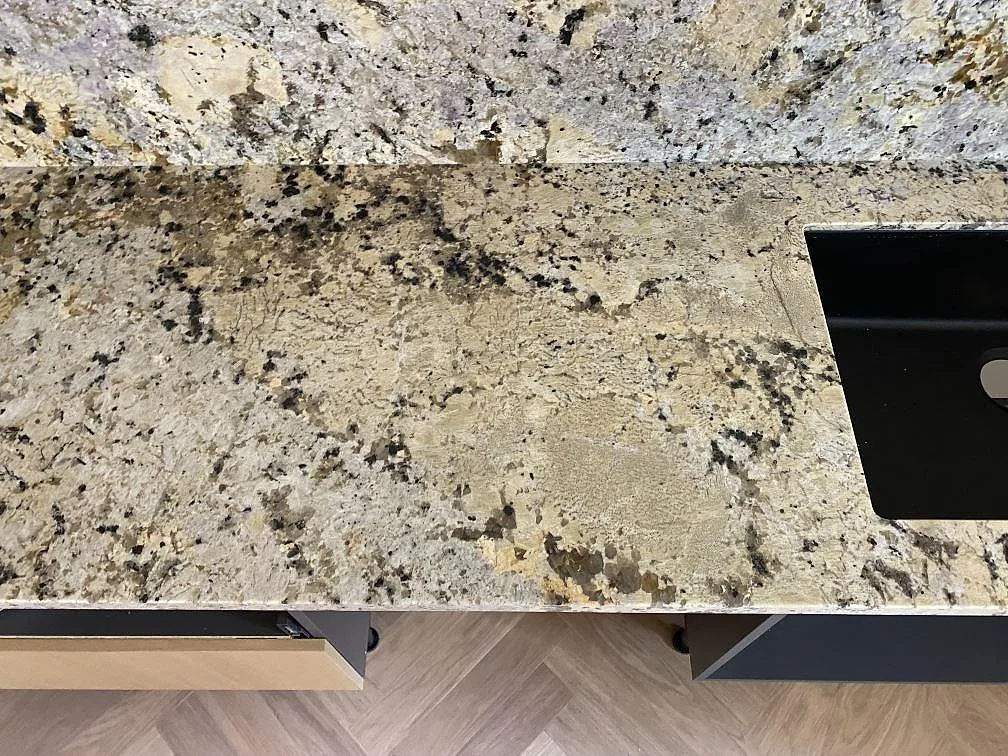 Detalj av polerad Alaskan white granit vid diskho och stänkskydd, med ljus och mörk ådring i Höllviken.