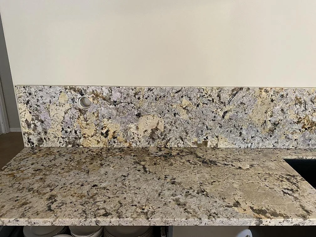 Närbild av stänkskydd och bänkskiva i polerad Alaskan white granit med grå och varma mineralfält i Höllviken.