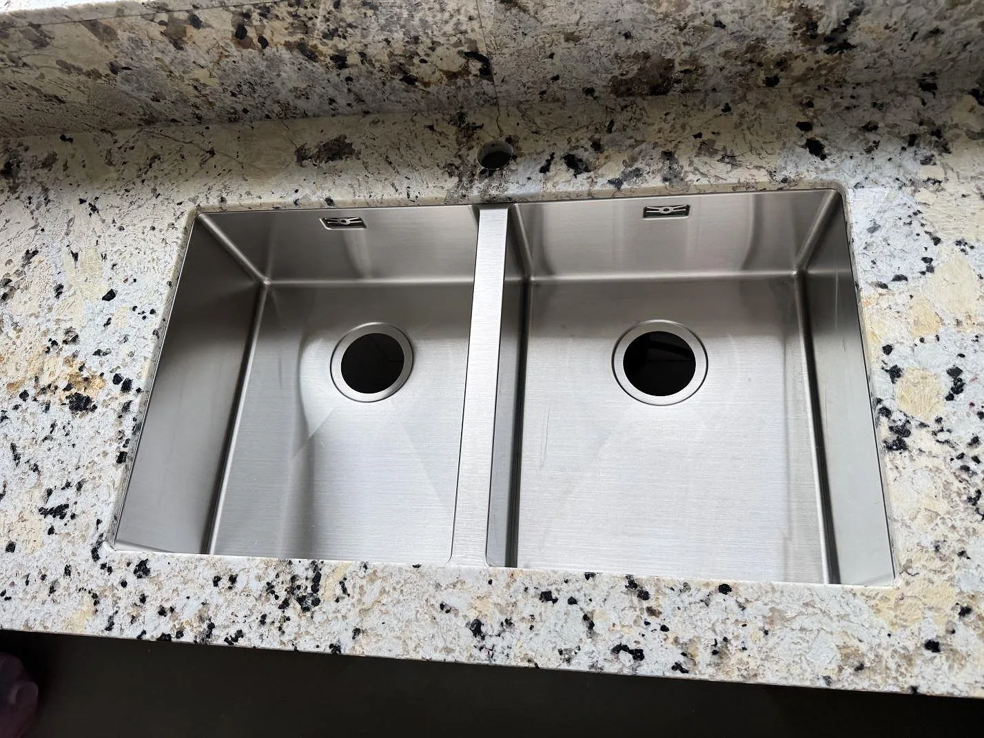 Detalj av polerad Alaskan white granit runt en dubbel rostfri diskho i kök i Kristianstad.