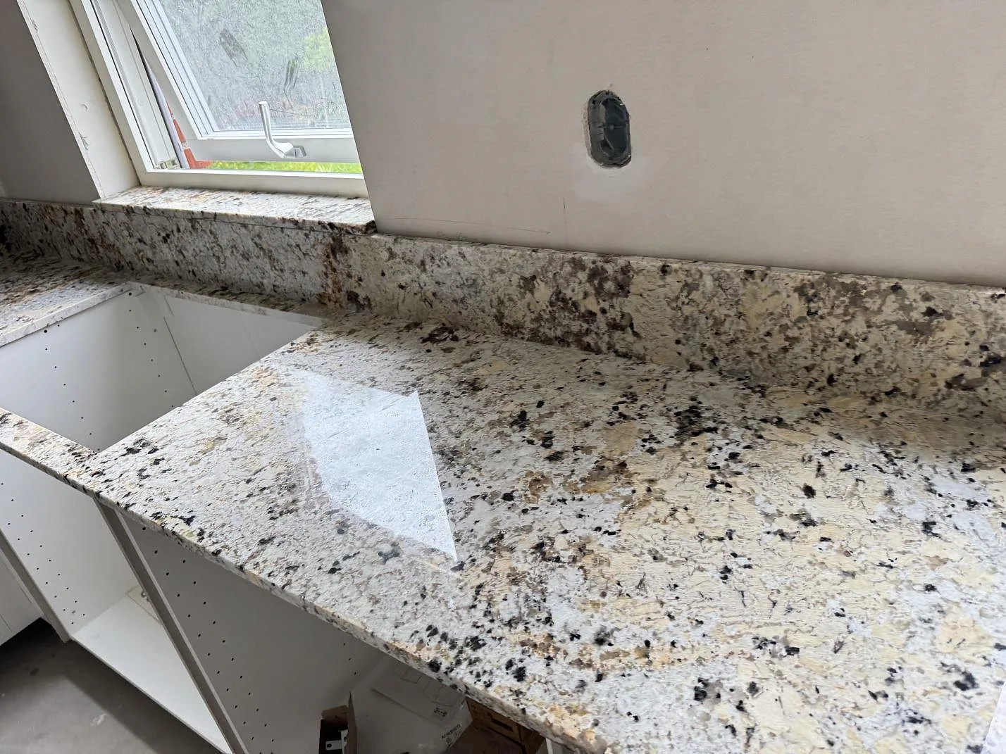 Lång bänkyta i polerad Alaskan white granit med stänkkant och fönsterbänk under montering i Kristianstad.