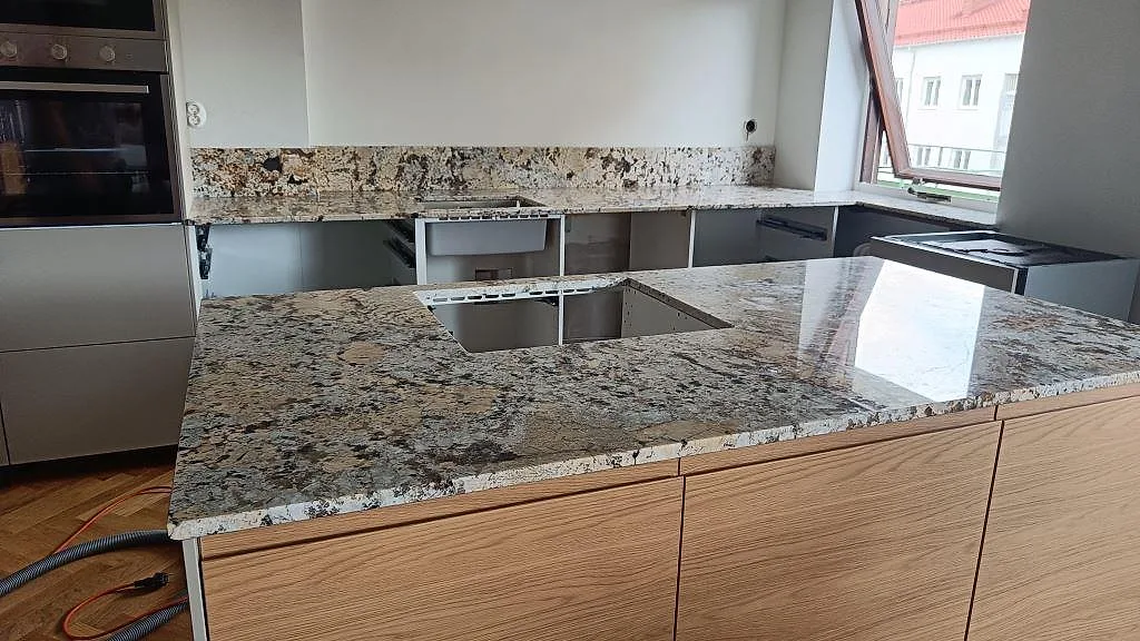 Köksbänkskiva i polerad Alaskan white granit med köksö, öppning för häll och stänkskydd i ett kök i Malmö.