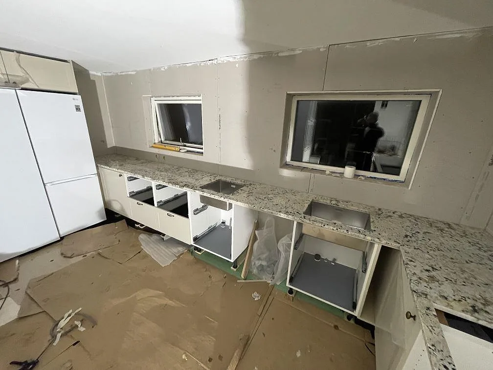 Lång köksbänkskiva i polerad Alaskan white granit med två underlimmade rostfria hoar i ett kök under montering i Svartsjö.
