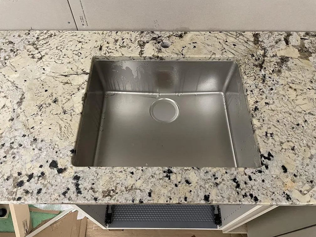 Detalj av rostfri diskho under en polerad Alaskan white granitbänkskiva med synlig mineralteckning i Svartsjö.