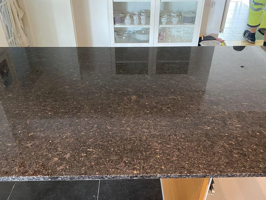 Närbild av polerad Angola Black granit på köksö med mörk spegling och mineralspel i Eslöv.