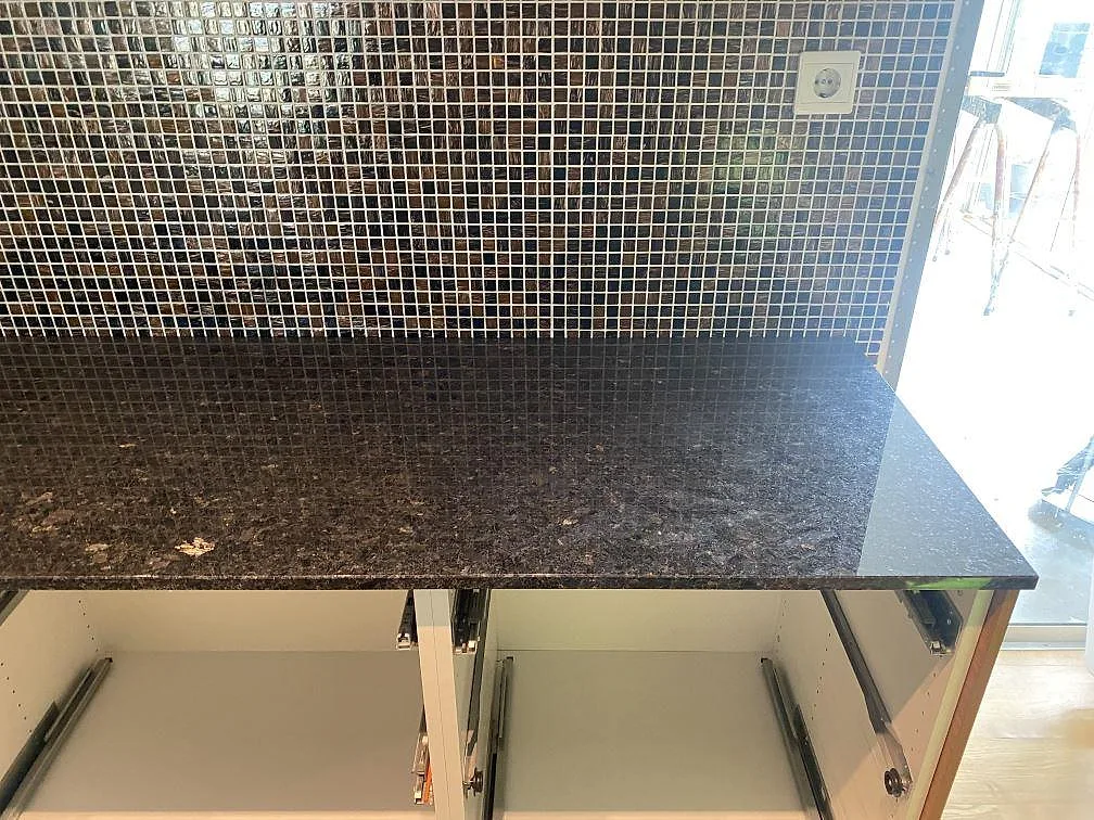 Polerad Angola Black granit framför mörk mosaikvägg och öppna vita stommar i Eslöv.