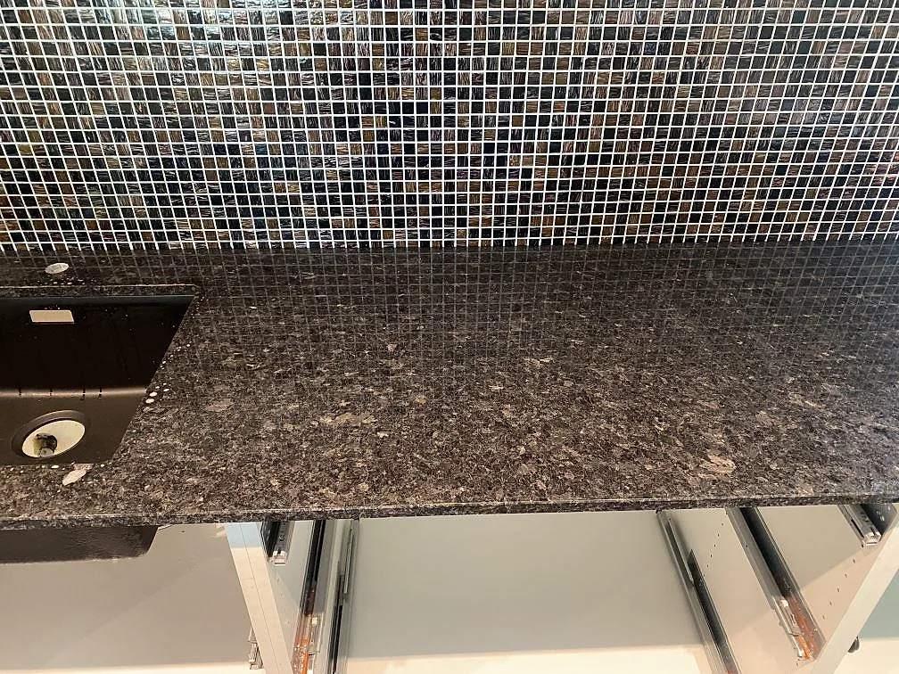 Detalj av polerad Angola Black granit bredvid svart diskho och mörkt mosaikstänkskydd i Eslöv.