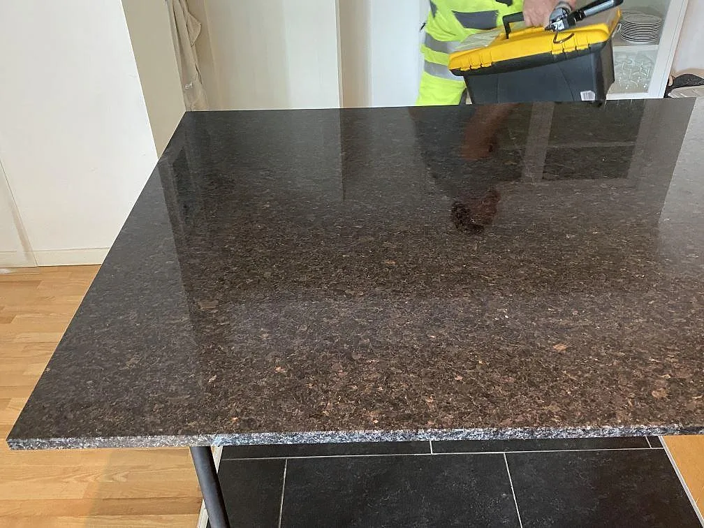 Polerad köksö i Angola Black granit med mörk blank yta och installatör i bakgrunden i Eslöv.