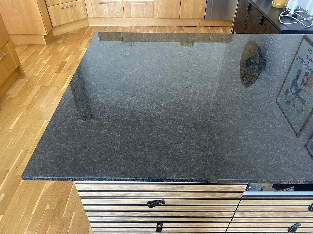 Polerad Angola Black granit som köksö sedd ovanifrån, med tydlig melering och reflektioner, i ett kök i Hässleholm.