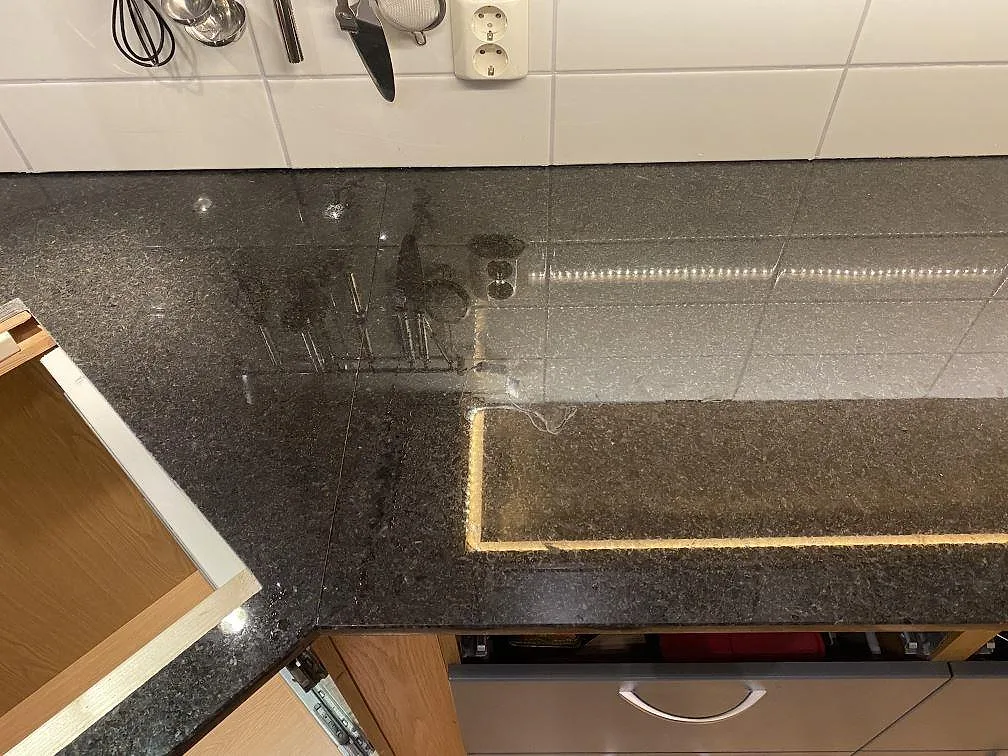 Detalj av polerad Angola Black granit vid hällplatsen med speglingar från kakel och belysning i Hässleholm.
