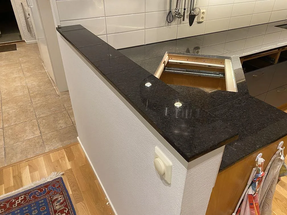 Sidovy av polerad Angola Black granit på köksbänk och kort bänkskiva mot halvö i Hässleholm.