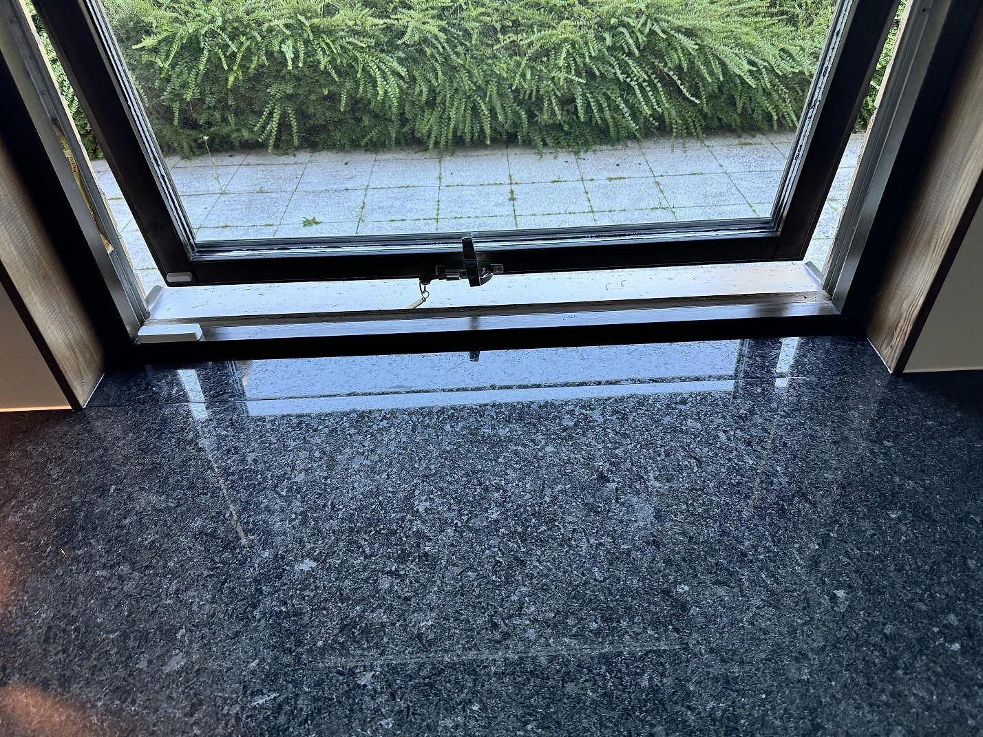 Detalj av blank Angola Black granit vid fönster, polerad mörk köksbänkskiva med tät mineralteckning i HJÄRUP.
