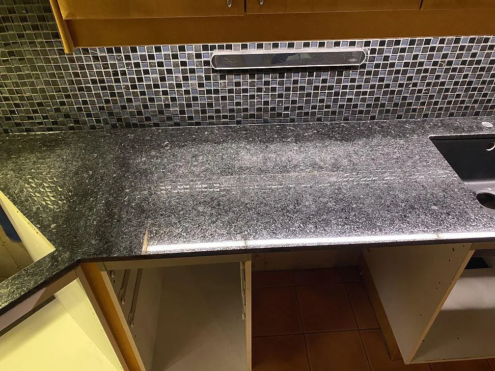 Rak arbetsyta i polerad Angola Black granit med mosaikvägg och diskho vid kanten i ett kök i Höllviken.