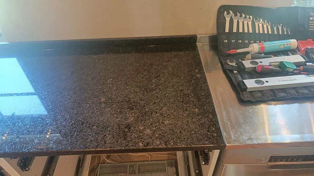 Detalj av polerad Angola Black granit vid hällsida, verktyg och rostfri arbetsyta i kök i Lund.