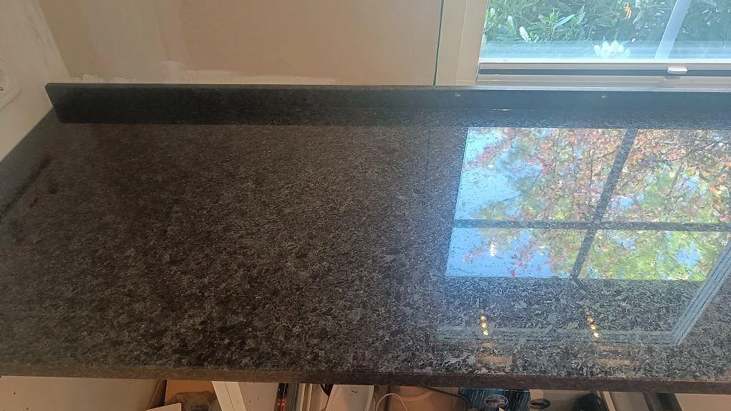Polerad Angola Black granit under fönster med mörk stänkkant och synlig naturstensstruktur i Lund.