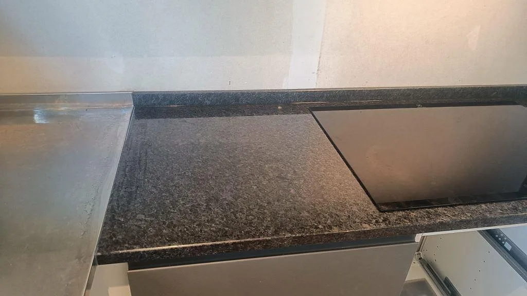 Hällområde i köksbänkskiva av polerad Angola Black granit intill rostfri arbetsyta i Lund.