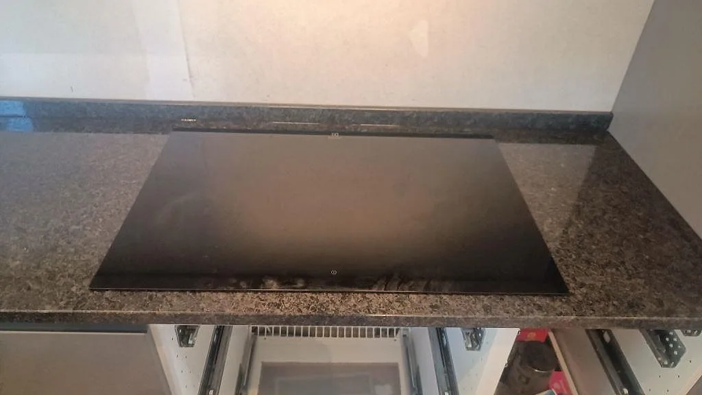Häll infälld i polerad Angola Black granit med mörk stänkkant i ett kök under montering i Lund.