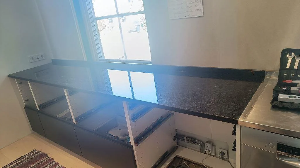 Köksbänkskiva i polerad Angola Black granit med låg stänkkant vid fönster i ett kök i Lund.
