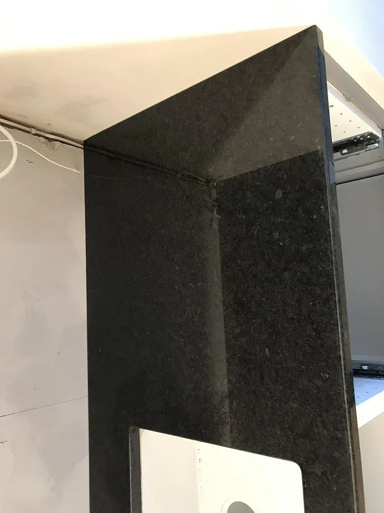L-formad svart Angola Black-granitbänkskiva med underlimmad diskho mot obeklädd vägg i ett kök i Malmö.
