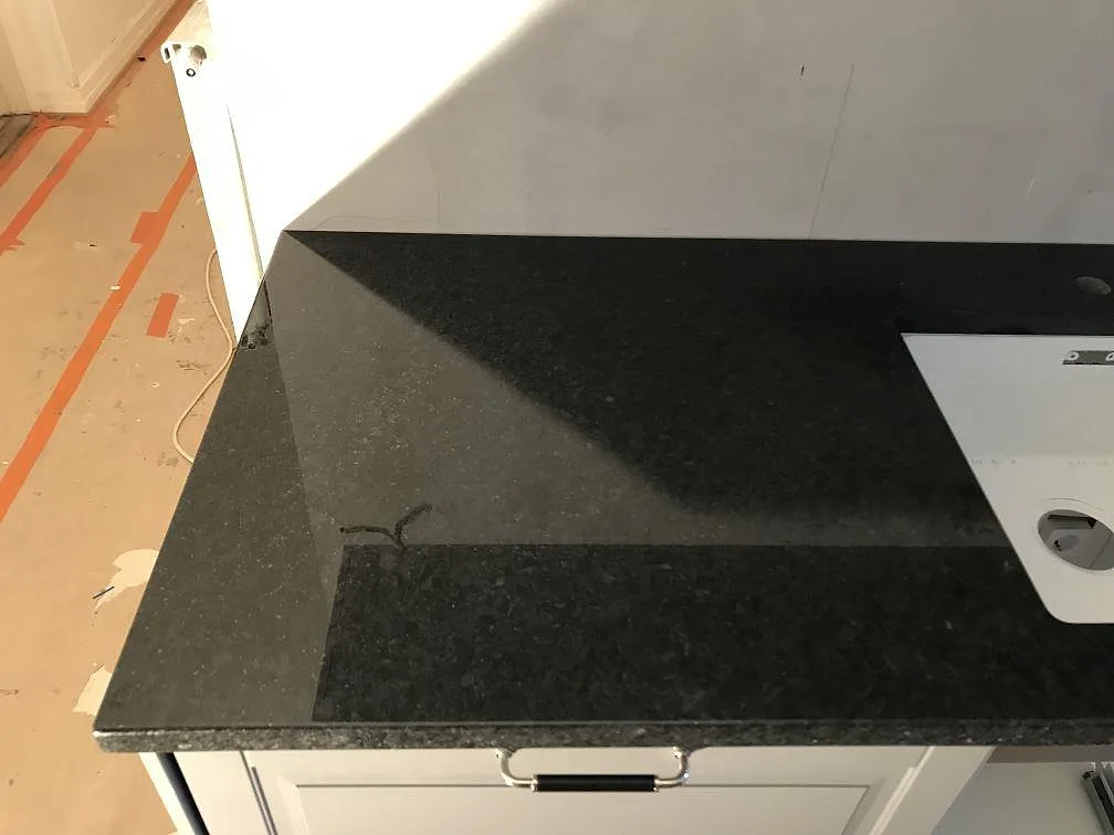 Hörn av polerad svart Angola Black-granitbänkskiva med kromat bygelhandtag och vit underlimmad diskho i ett kök i Malmö.