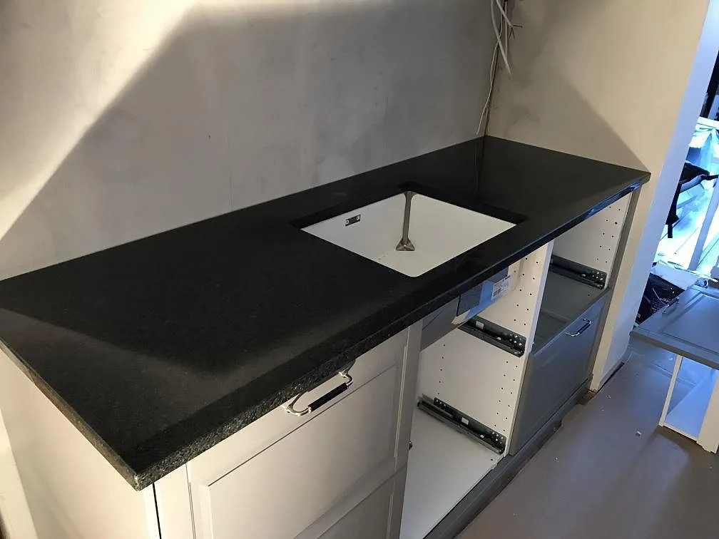 Köksbänkskiva i svart Angola Black-granit med vit underlimmad diskho och vit Shaker-inredning i ett kök under montering i Malmö.