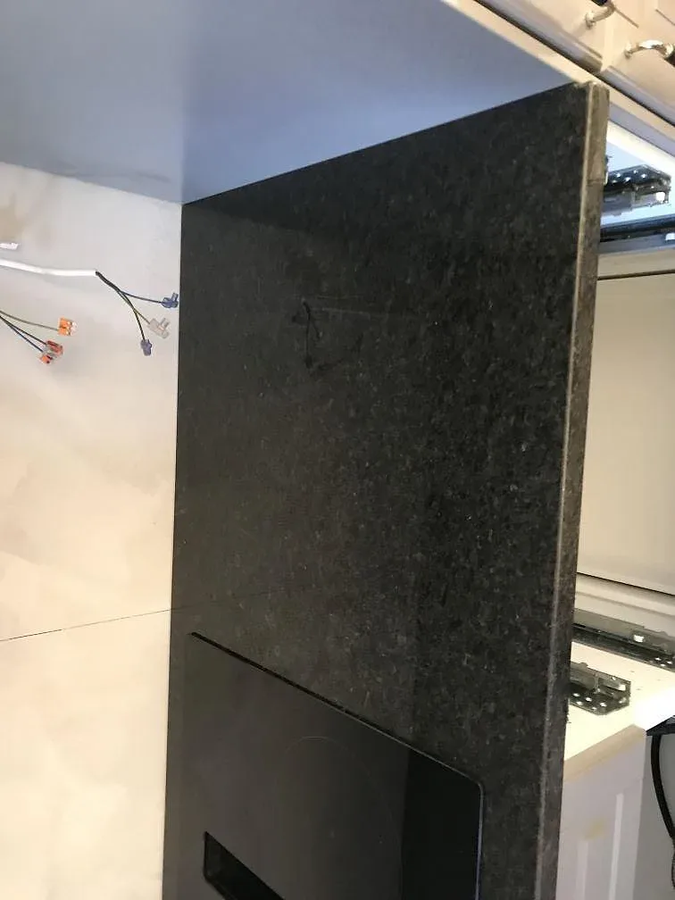 Svart Angola Black-granitbänkskiva med urtag för induktionshäll och framdragen el under montering i ett kök i Malmö.