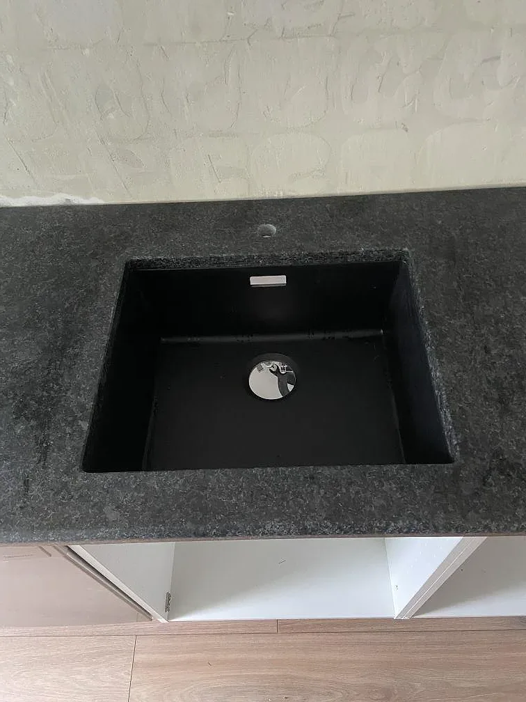 Underlimmad svart komposithho med krombrandare i en bänkskiva av Angola Black granit i ett kök i Malmö.