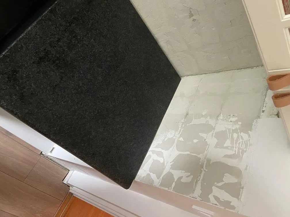 Hörnparti av köksbänkskiva i Angola Black granit med svart induktionshäll mot omålad vägg i ett kök i Malmö.