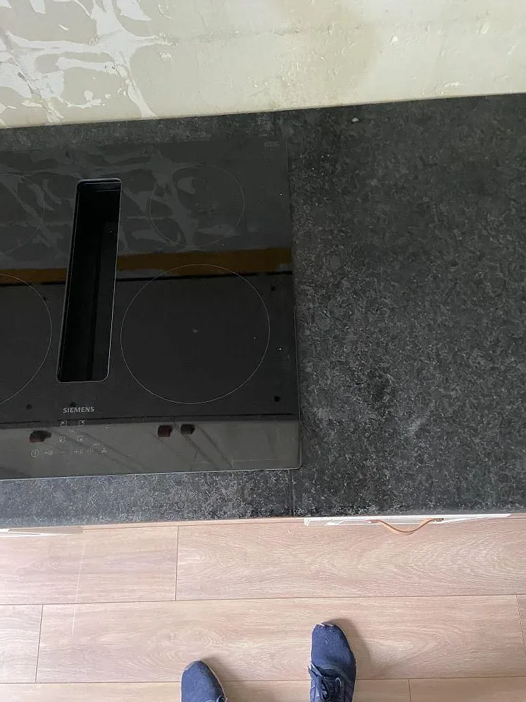 Mörk Angola Black granitbänk med installerad svart induktionshäll och ljust ekfärgat golv i ett kök i Malmö.