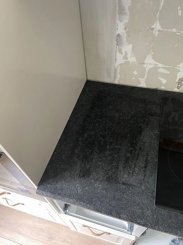 Närbild på Angola Black granit som köksbänkskiva med uppvikt stänkkant och induktionshäll i ett kök i Malmö.