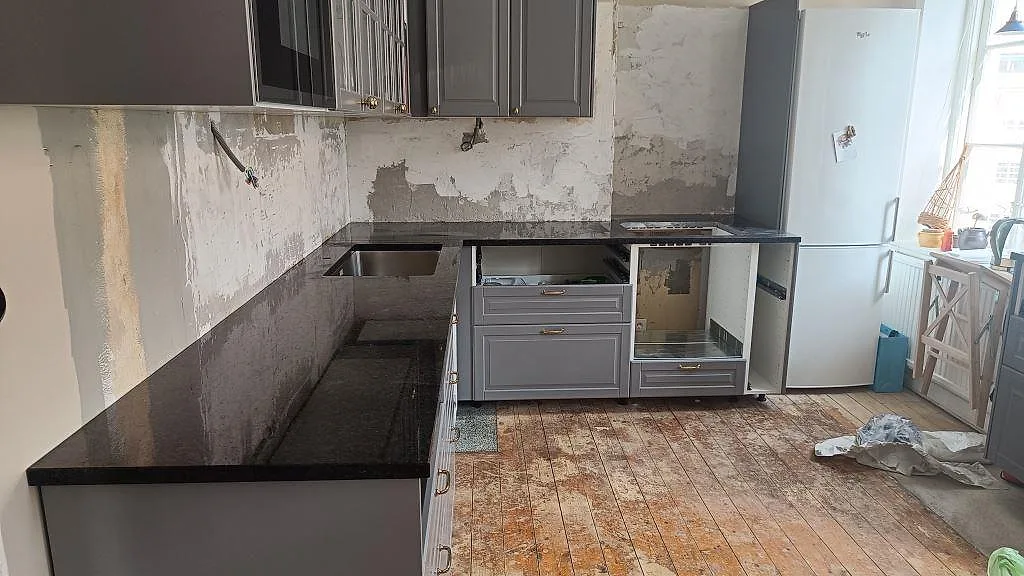 Köksbänkskiva i 30 mm polerad Angola Black-granit i ett kök i Malmö, med rostfri diskho och förberett hälluttag under montering.