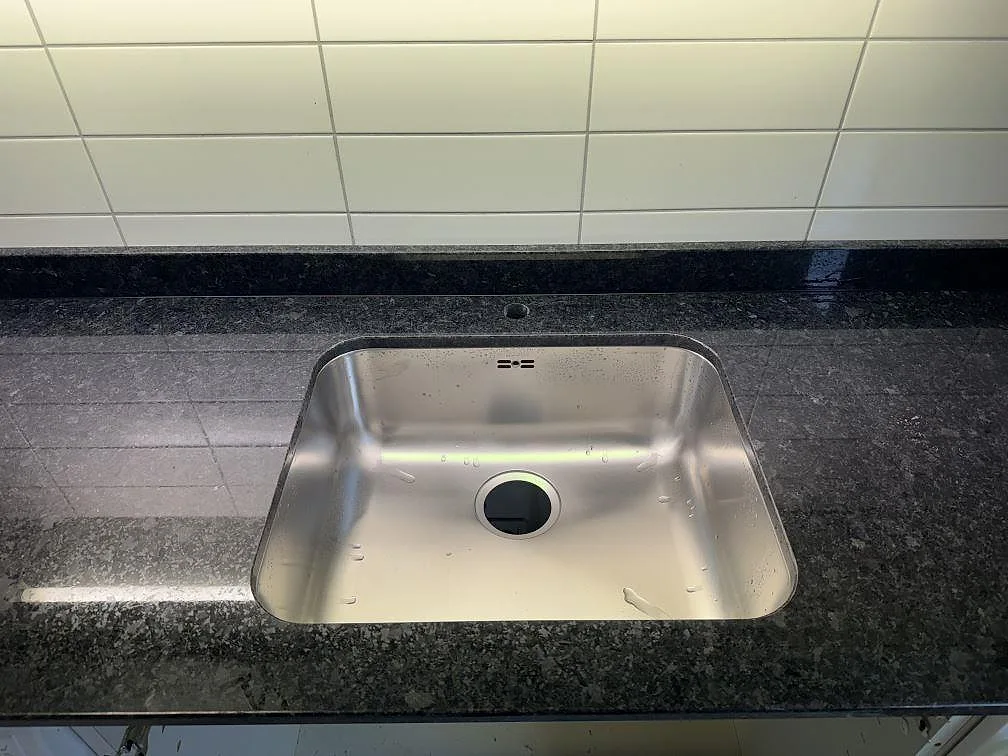 Närbild på polerad bänkskiva i Angola Black granit med rostfri diskho och mörk stenkant i Malmö.