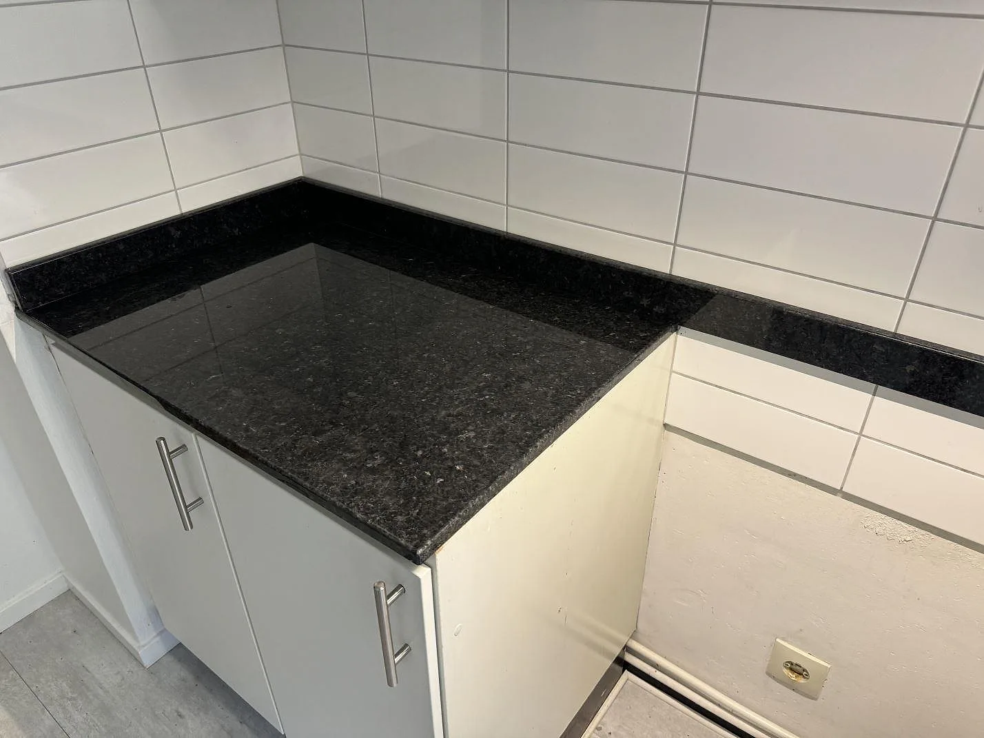 Polerad Angola Black granit på kort bänkyta i kök med vita stommar och kaklad vägg i Malmö.
