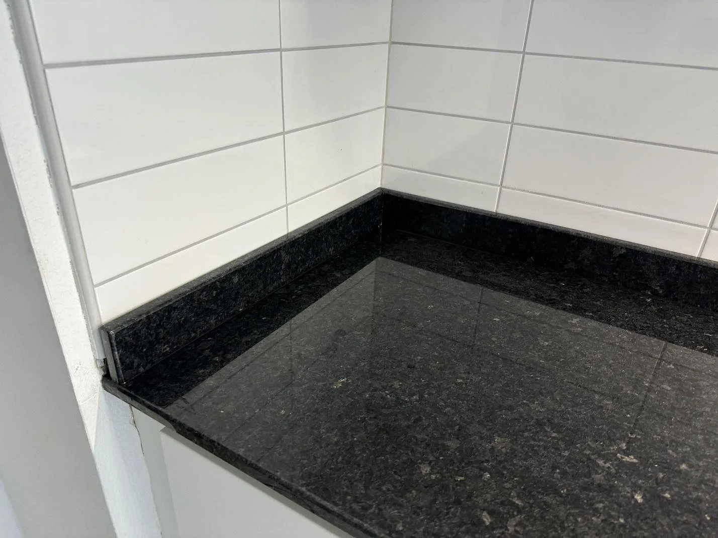 Detalj av mörk Angola Black granit i ett kökshörn med blank yta och uppvikt stenkant i Malmö.