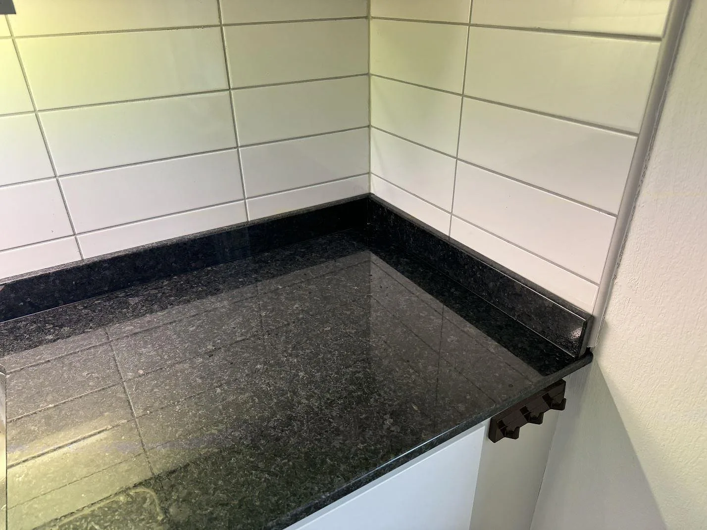 Hörn av köksbänkskiva i polerad Angola Black granit med svart stenkant mot vitt kakel i Malmö.