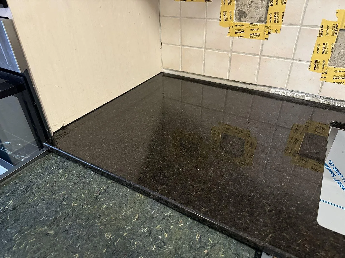 Polerad köksbänkskiva i Angola Black granit med speglad mörk yta mot kaklad vägg i ett kök i Malmö.