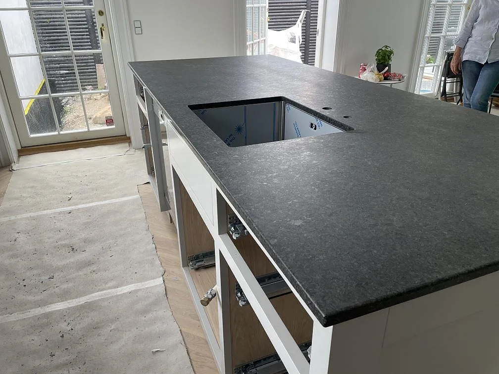 Närbild av köksö i matt Angola Black granit med underlimmad rostfri diskho och borrade hål för blandare i Rungsted Kyst.