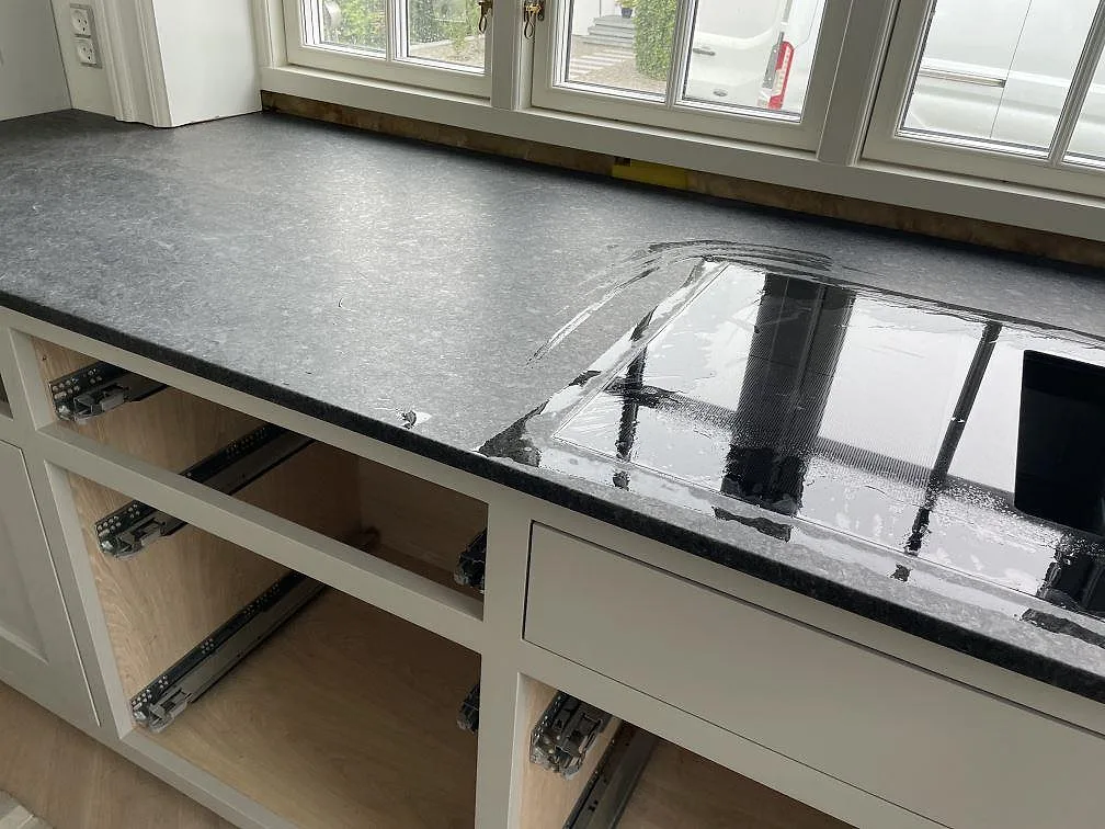 Detalj av svart induktionshäll i bänkskiva av matt Angola Black granit under montering i Rungsted Kyst.