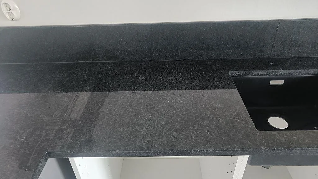 Närbild på köksbänk i svart Angola Black granit med uppvikt stänkkant mot vägg i ett kök i Staffanstorp.