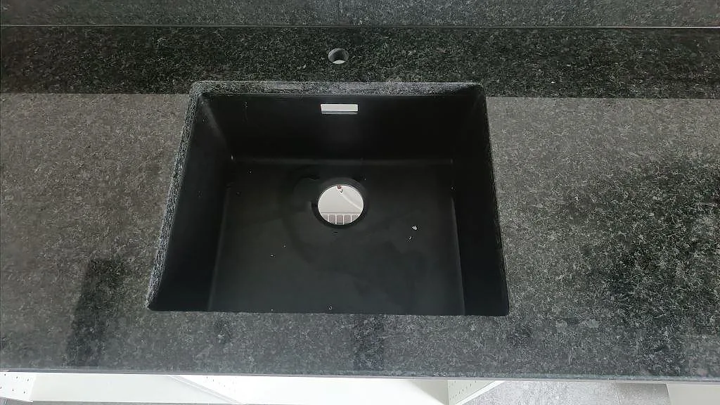 Underlimmad svart kompositdiskho i köksbänk av svart Angola Black granit i ett kök i Staffanstorp.