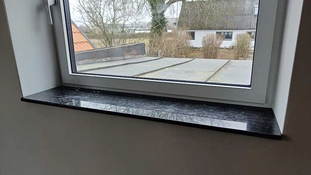 Bred fönsterbänk i svart Angola Black granit, polerad, med spegelblank yta i Staffanstorp.