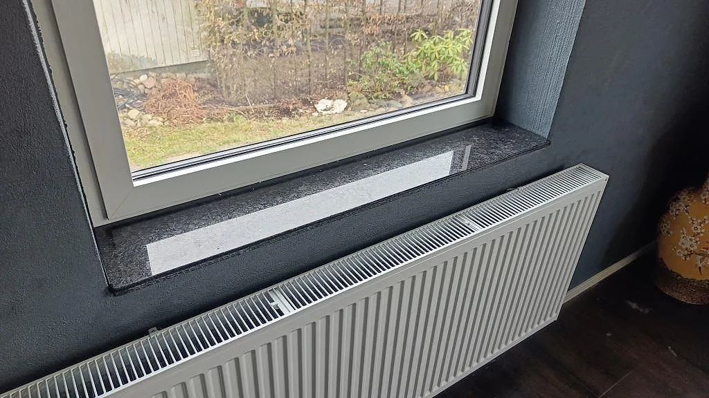 Fönsterbänk i polerad Angola Black granit ovanför en radiator i ett rum i Staffanstorp.