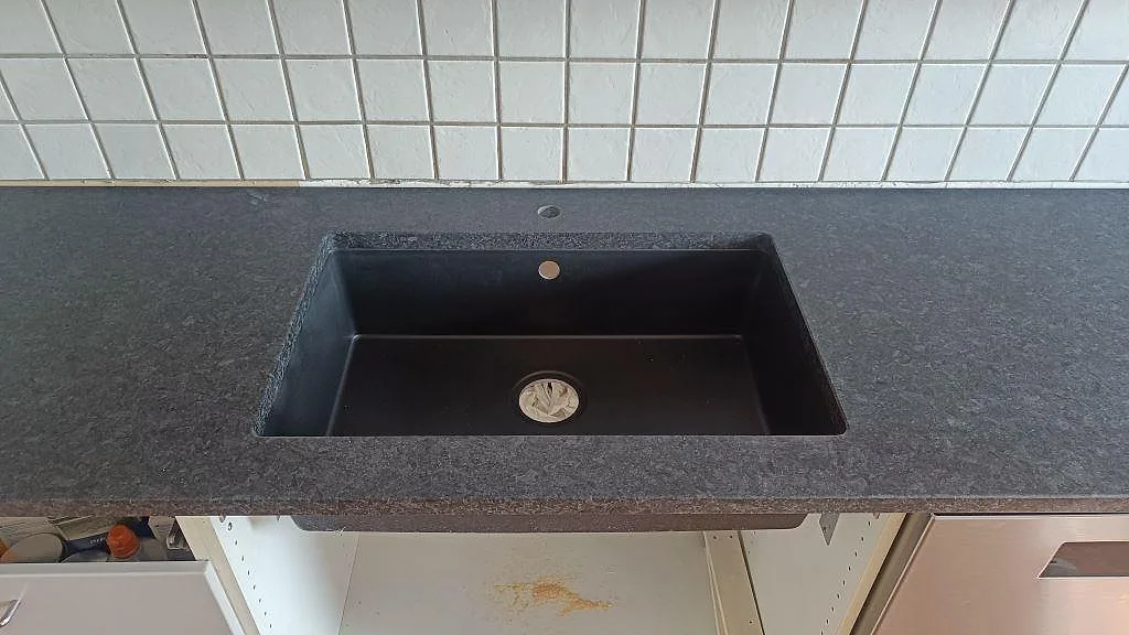 Närbild på svart diskho monterad under en matt köksbänkskiva i Angola Black granit i Staffanstorp.