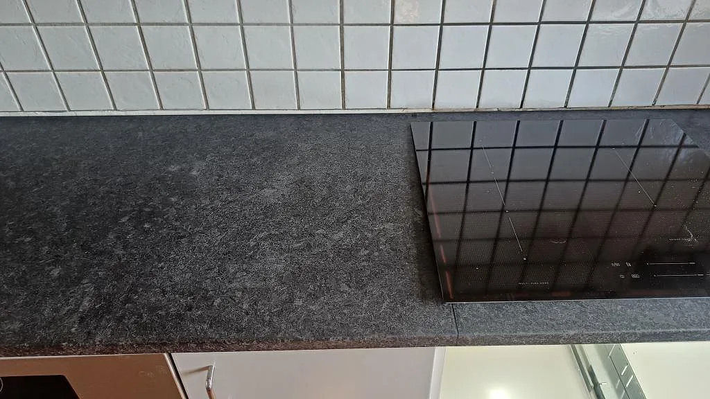 Köksbänkskiva i matt Angola Black granit med svart induktionshäll infälld i arbetsytan i Staffanstorp.