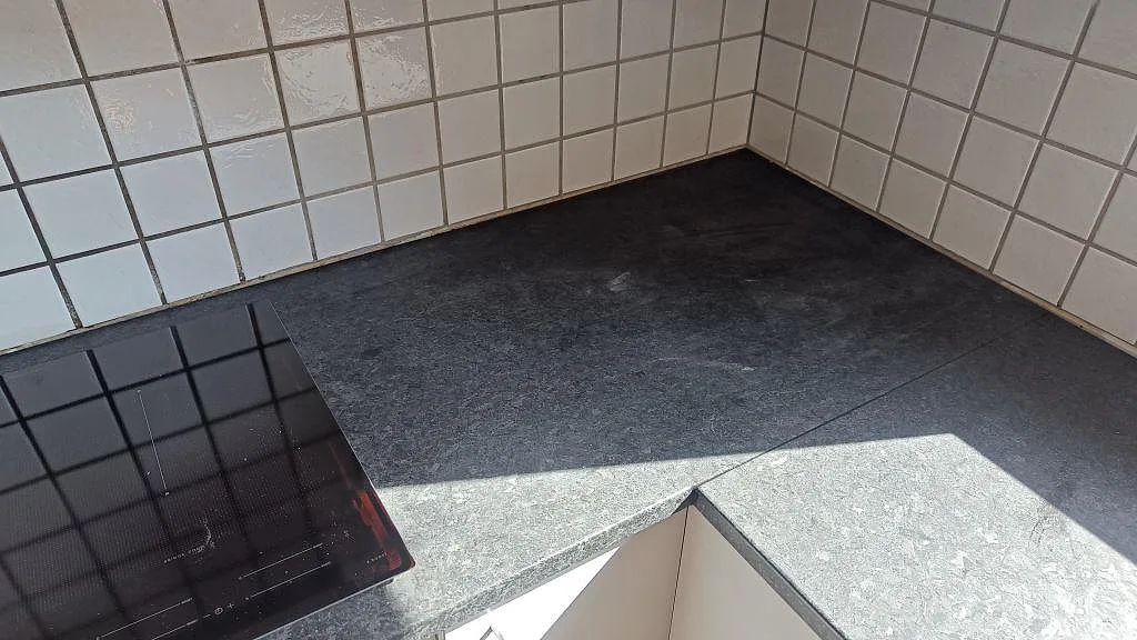 U-format hörn med matt Angola Black granit, induktionshäll och ljusinsläpp över köksbänken i Staffanstorp.