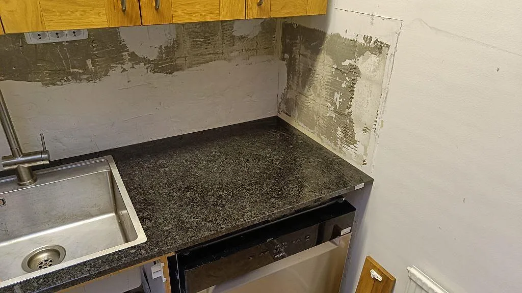 Höger del av köksbänkskiva i polerad Angola Black granit intill diskmaskin och vägg under montering i Tibro.