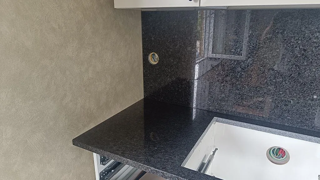 Hörnvy av polerad Angola Black granit med underlimmad diskho och blank stänkvägg i kök i Tomelilla.