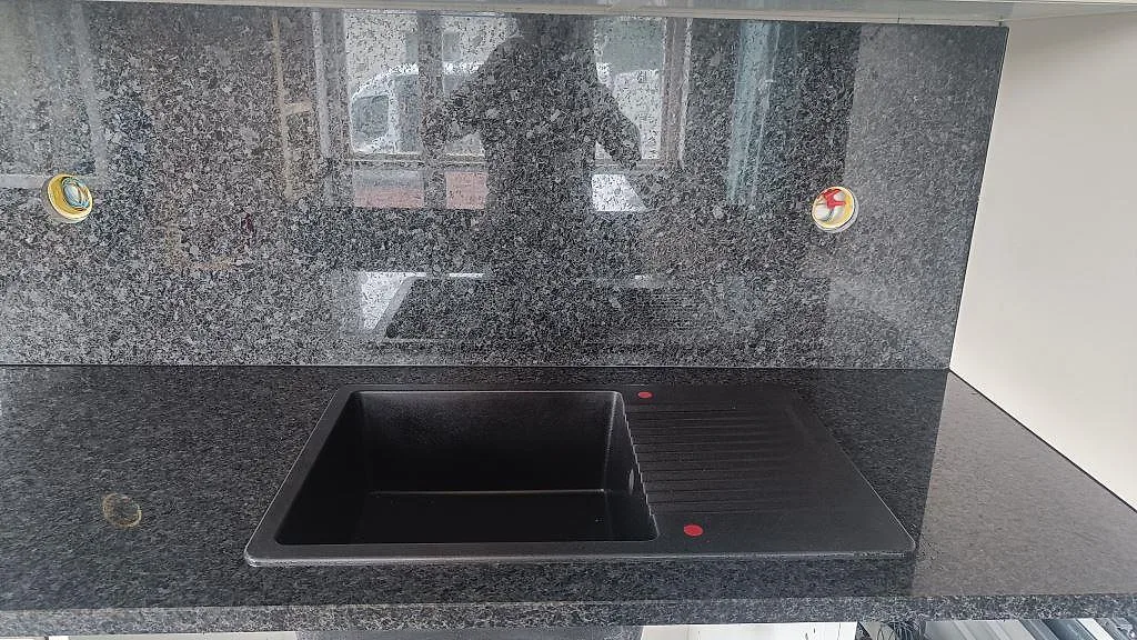 Detalj av mörk diskho i polerad Angola Black granit med stänkvägg under överskåp i Tomelilla.
