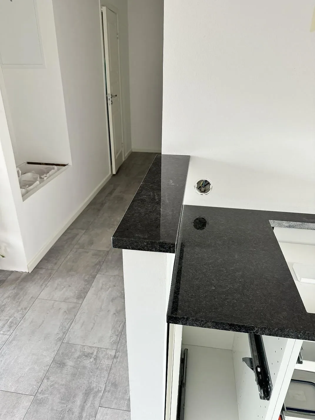 Detalj av köksbänkskiva i Angola Black granit med uppvikt kant och öppna vita stommar under montering i Vellinge.